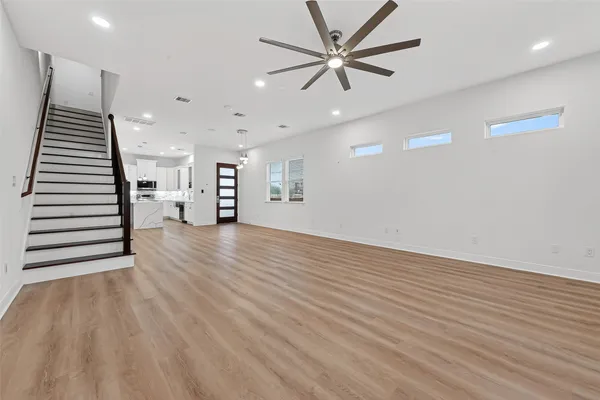 an empty room with wooden floor chandelier fan and windows