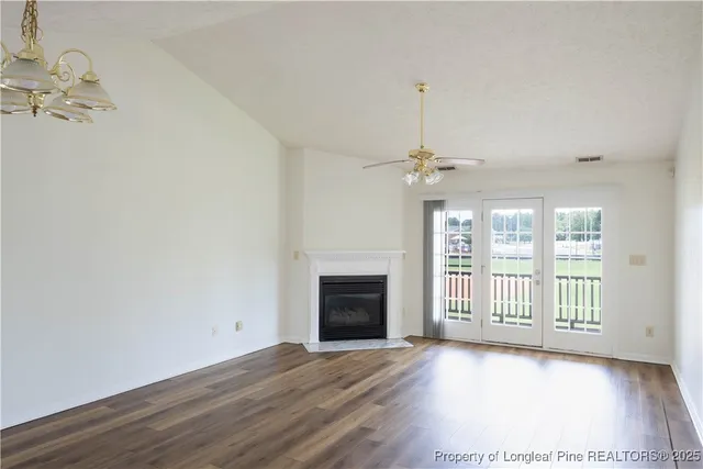 an empty room with wooden floor chandelier and windows