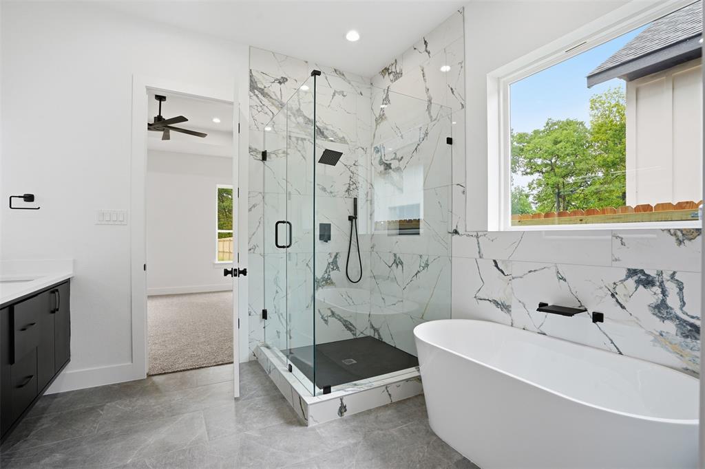 1111 Riverwood Road Dallas, TX 75217 - Photo 22 of 40 Modern bathroom featuring a freestanding soaking tub, a frameless glass shower enclosure with marble-look tile surround and black fixtures, and a contemporary vanity with a white countertop