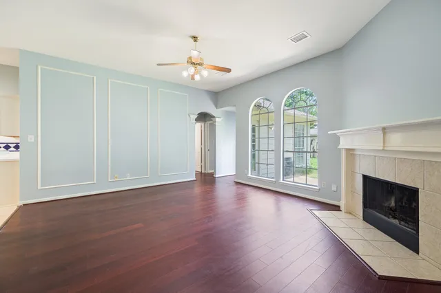 an empty room with wooden floor fireplace chandelier and windows