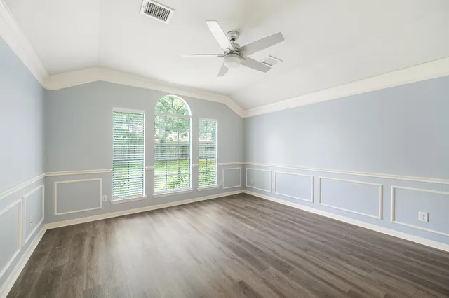 an empty room with wooden floor fan and windows
