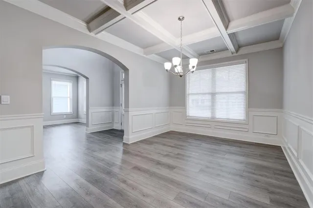 an empty room with wooden floor chandelier and windows
