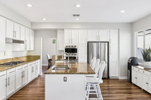 a kitchen with stainless steel appliances granite countertop a stove top oven a sink dishwasher and white cabinets with wooden floor