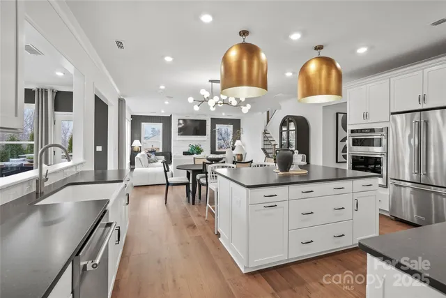 a kitchen with stainless steel appliances kitchen island granite countertop a stove a sink a refrigerator and white cabinets with wooden floor