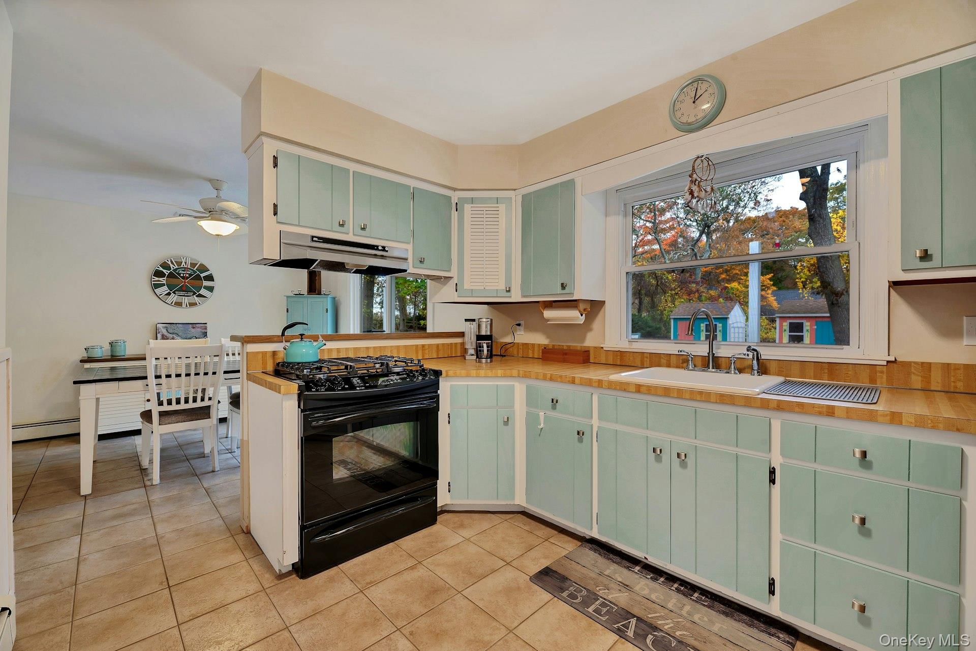 210 3rd Street Laurel, NY 11948 - Photo 9 of 22 Kitchen featuring green cabinetry, light tile patterned flooring, black gas range oven, under cabinet range hood, and a peninsula