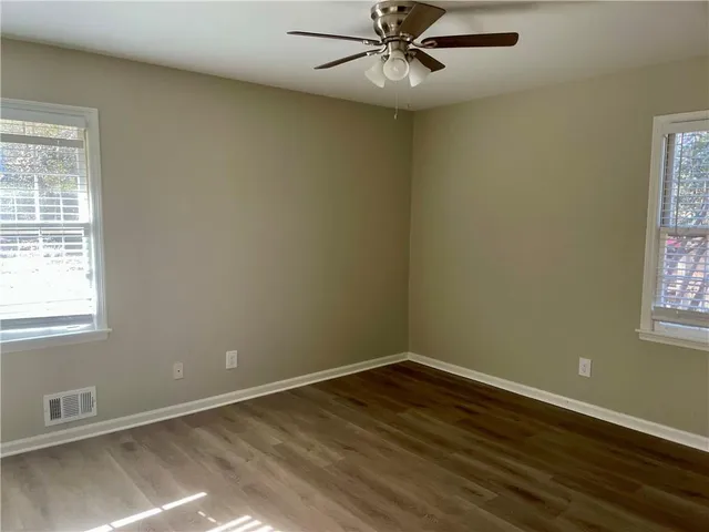 an empty room with wooden floor fan and windows