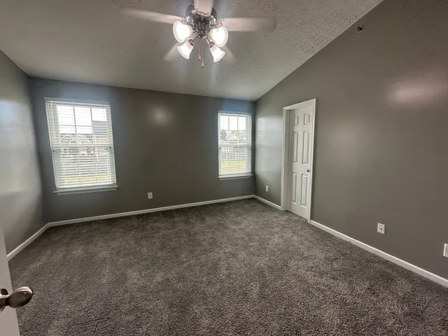 an empty room with windows and chandelier fan