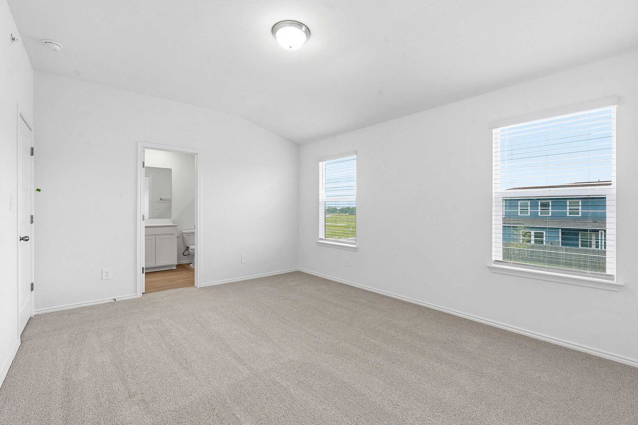 164 Cinnabar Lane, Unit 4 Kyle, TX 78640 - Photo 12 of 23 Spacious room featuring carpeting, two windows with blinds, a ceiling-mounted light fixture, and a doorway to a private bathroom with a vanity and toilet