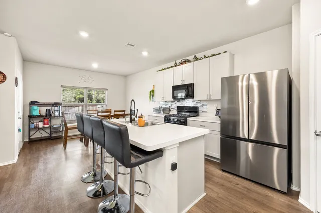 a kitchen with stainless steel appliances a refrigerator a stove a sink dishwasher a dining table and chairs with wooden floor