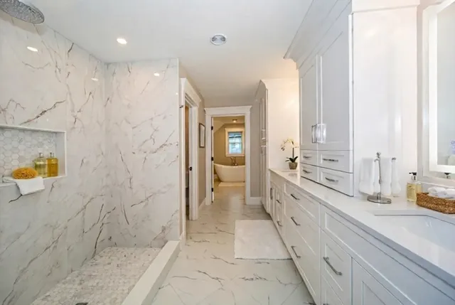 a large white bathroom with a granite countertop sink a mirror a bathtub and shower