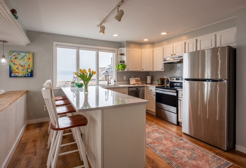 4 N Road, Unit 2 Rockport, MA 01966 - Photo 8 of 21 a kitchen with stainless steel appliances granite countertop a refrigerator a stove a sink a dining table and chairs with wooden floor