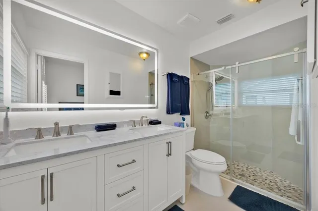 a bathroom with a double vanity sink toilet mirror and shower
