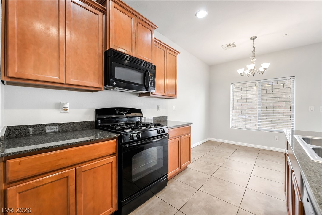 33 Jasmine Point Street Henderson, NV 89074 - Photo 10 of 36 Kitchen with black appliances, wood finish cabinets, suspended lighting, dark stone counters, and light tile patterned flooring