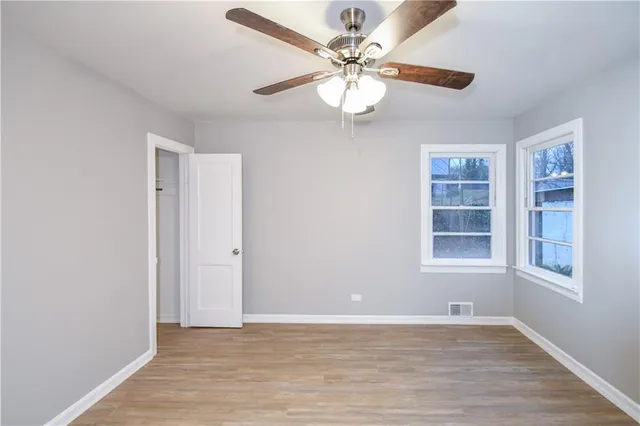 an empty room with wooden floor chandelier fan and windows