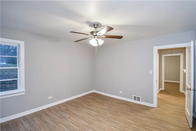 a view of an empty room with window a ceiling fan and wooden floor