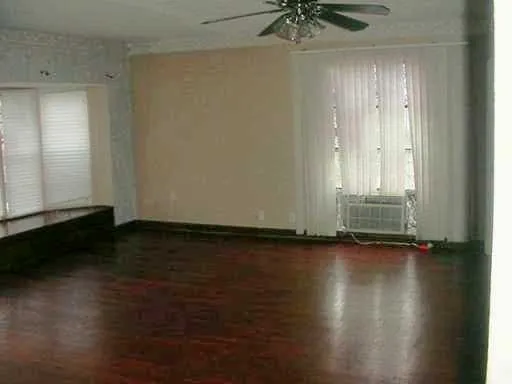 an empty room with wooden floor and windows with curtains