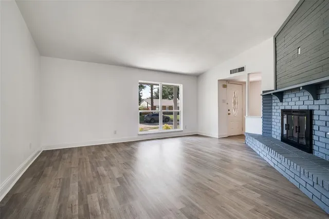an empty room with wooden floor fireplace and windows
