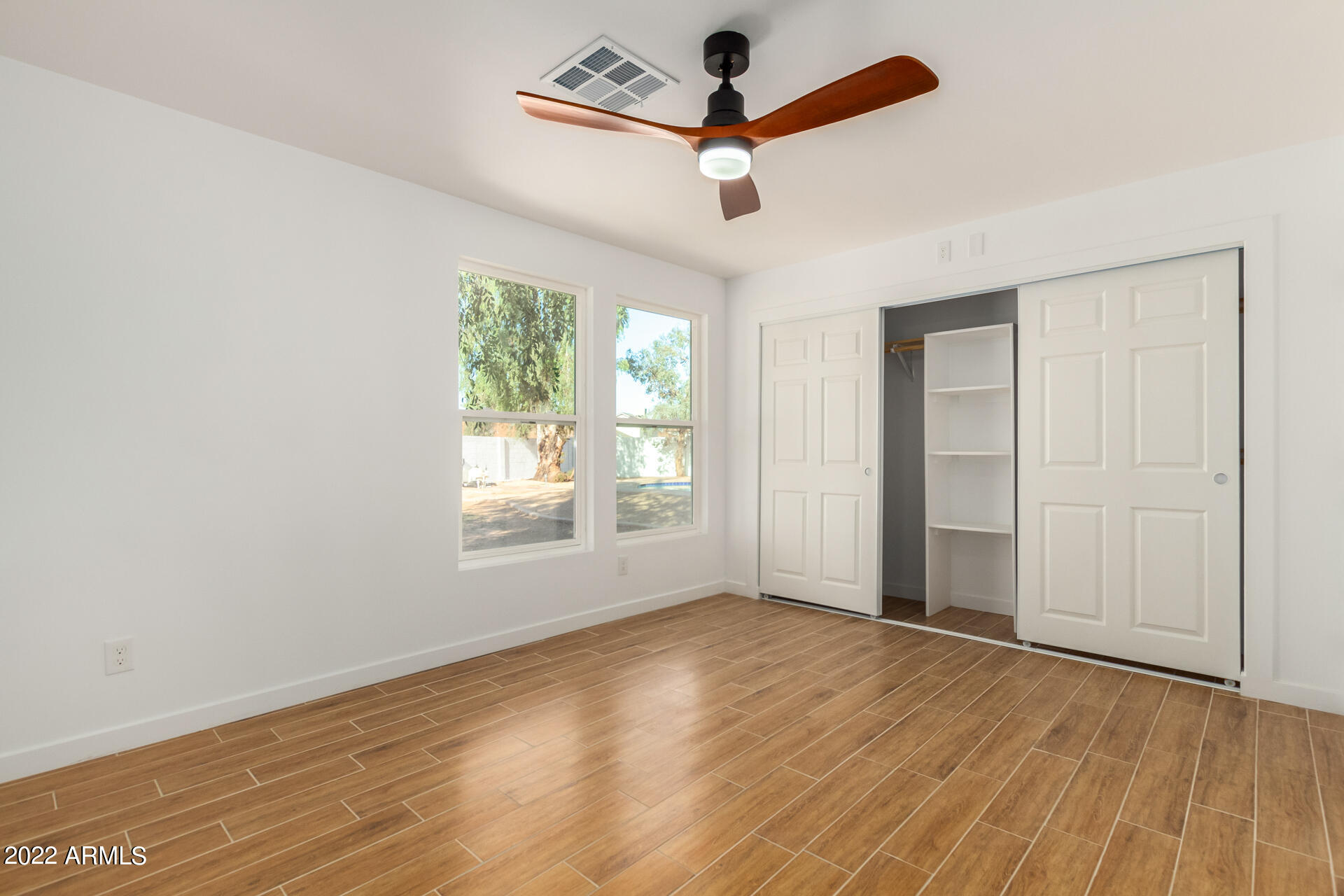 4110 East Vineyard Road Phoenix, AZ 85042 - Photo 19 of 31 an empty room with wooden floor chandelier fan and windows