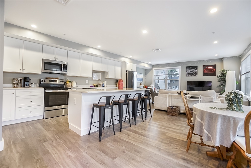 245 Bussey Street, Unit 205 Dedham, MA 02026 - Photo 1 of 17 a kitchen with a table chairs a sink dishwasher a stove and a dining table with wooden floor