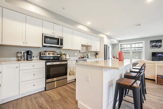a kitchen with stainless steel appliances kitchen island granite countertop a stove top oven a sink dishwasher and a refrigerator with wooden floor
