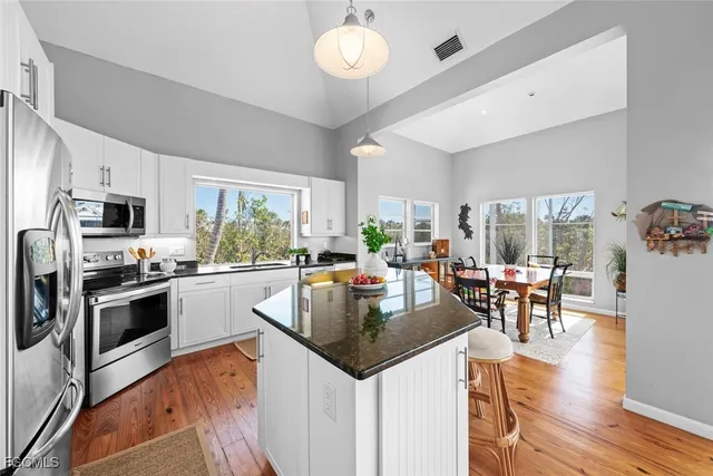 a kitchen with stainless steel appliances granite countertop a stove top oven a refrigerator a dining table and chairs with wooden floor