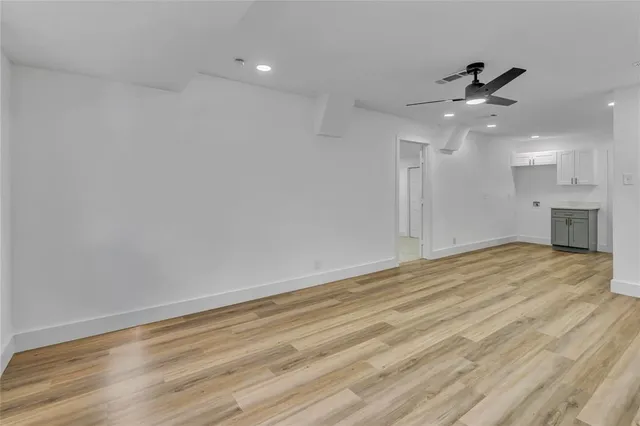an empty room with wooden floor a ceiling fan and kitchen view