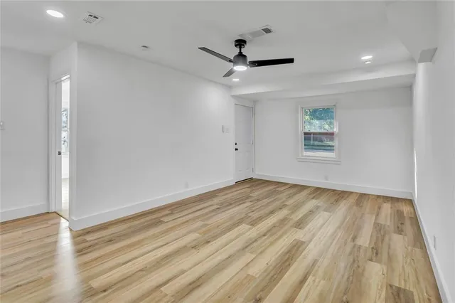 an empty room with wooden floor ceiling fan and windows