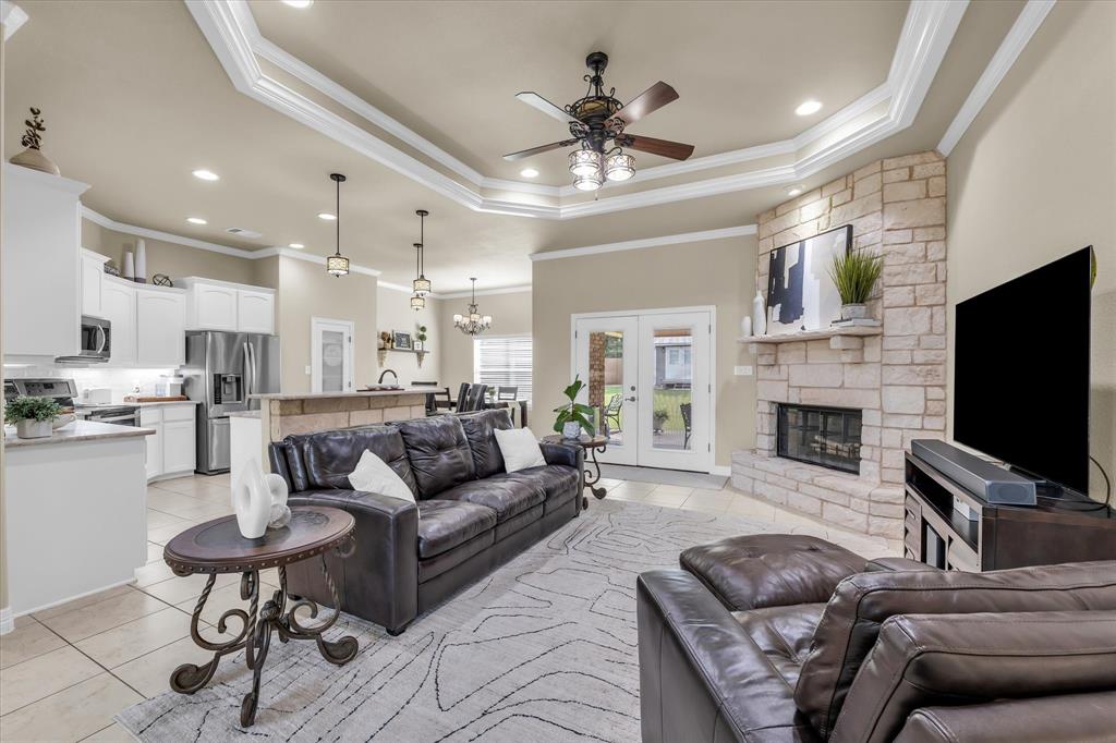 910 Springdale Lane Lorena, TX 76655 - Photo 5 of 39 Spacious living area featuring a corner stone fireplace, tray ceiling with crown molding, and tiled flooring