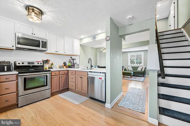 a kitchen with stainless steel appliances kitchen island granite countertop a stove top oven a sink dishwasher and white cabinets with wooden floor