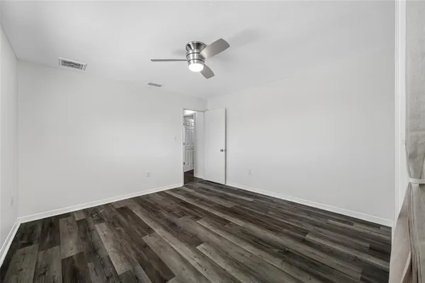 an empty room with wooden floor chandelier fan and windows