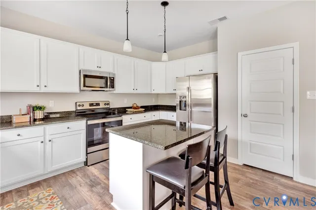a kitchen with stainless steel appliances granite countertop a sink a stove a refrigerator a microwave a dining table and chairs with wooden floor