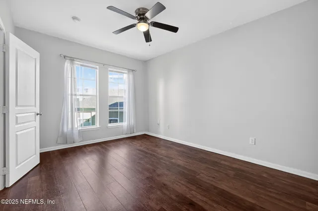 an empty room with wooden floor fan and windows