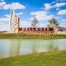 17439 Chester Valley Trail Hockley, TX 77447 - Photo 17 of 22 The photo shows an inviting entrance sign for the Dellrose community, featuring modern design elements and surrounded by landscaped greenery and a serene pond, under a bright blue sky.