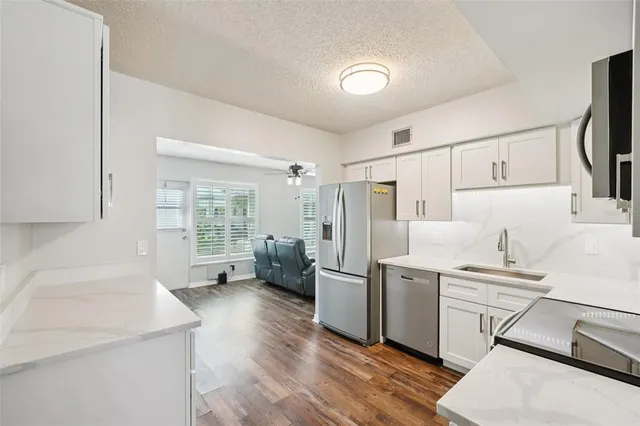 a kitchen with stainless steel appliances a refrigerator a sink a stove and white cabinets with wooden floor