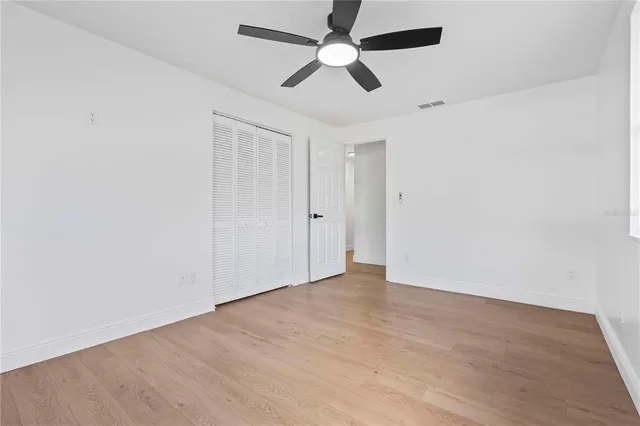an empty room with wooden floor ceiling fan and windows