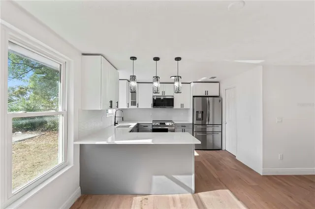 a large white kitchen with wooden floor and a large window