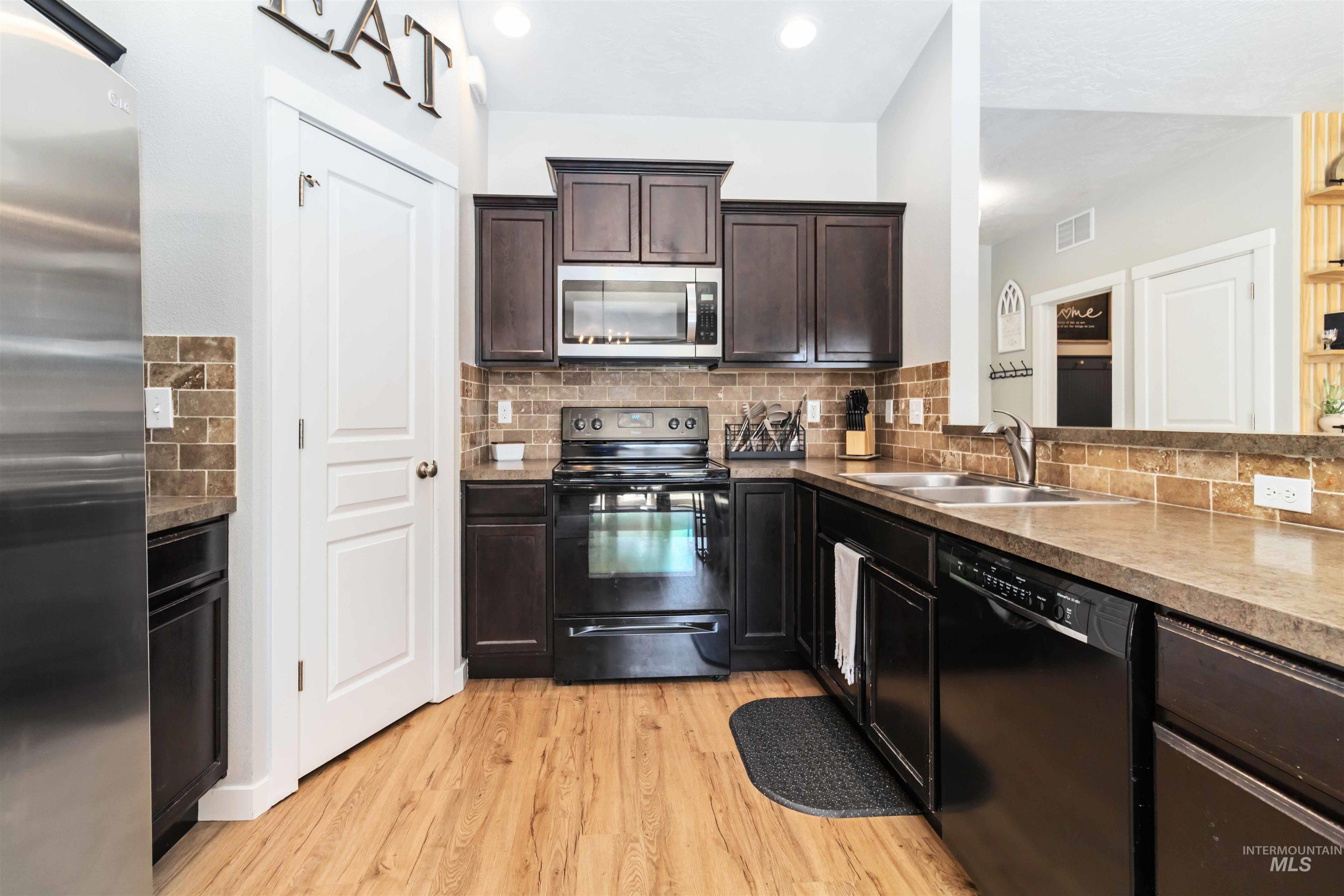 588 Gateway Avenue Middleton, ID 83644 - Photo 19 of 42 Kitchen featuring black appliances, dark wood finish cabinetry, light wood-style floors, decorative backsplash, and light countertops