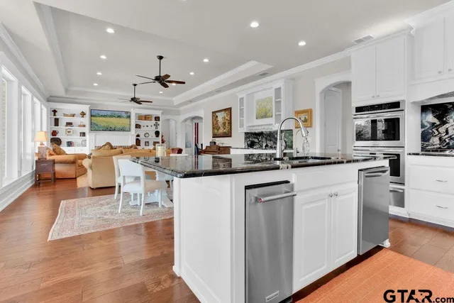a kitchen with stainless steel appliances kitchen island granite countertop a refrigerator oven stove a sink a dining table and chairs with wooden floor