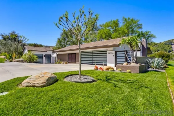 a house that has sitting in front of a big yard with potted plants