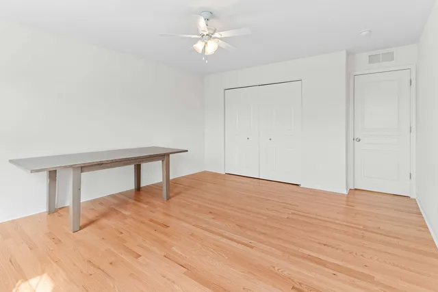 a view of an empty room with wooden floor and a ceiling fan