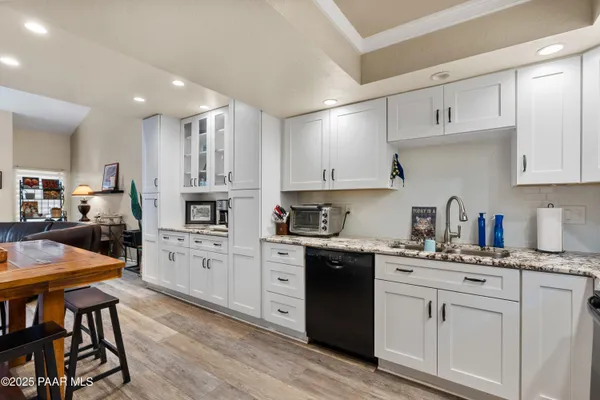 a kitchen with stainless steel appliances granite countertop a stove top oven a sink dishwasher and white cabinets with wooden floor