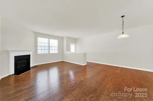 an empty room with wooden floor fireplace and windows