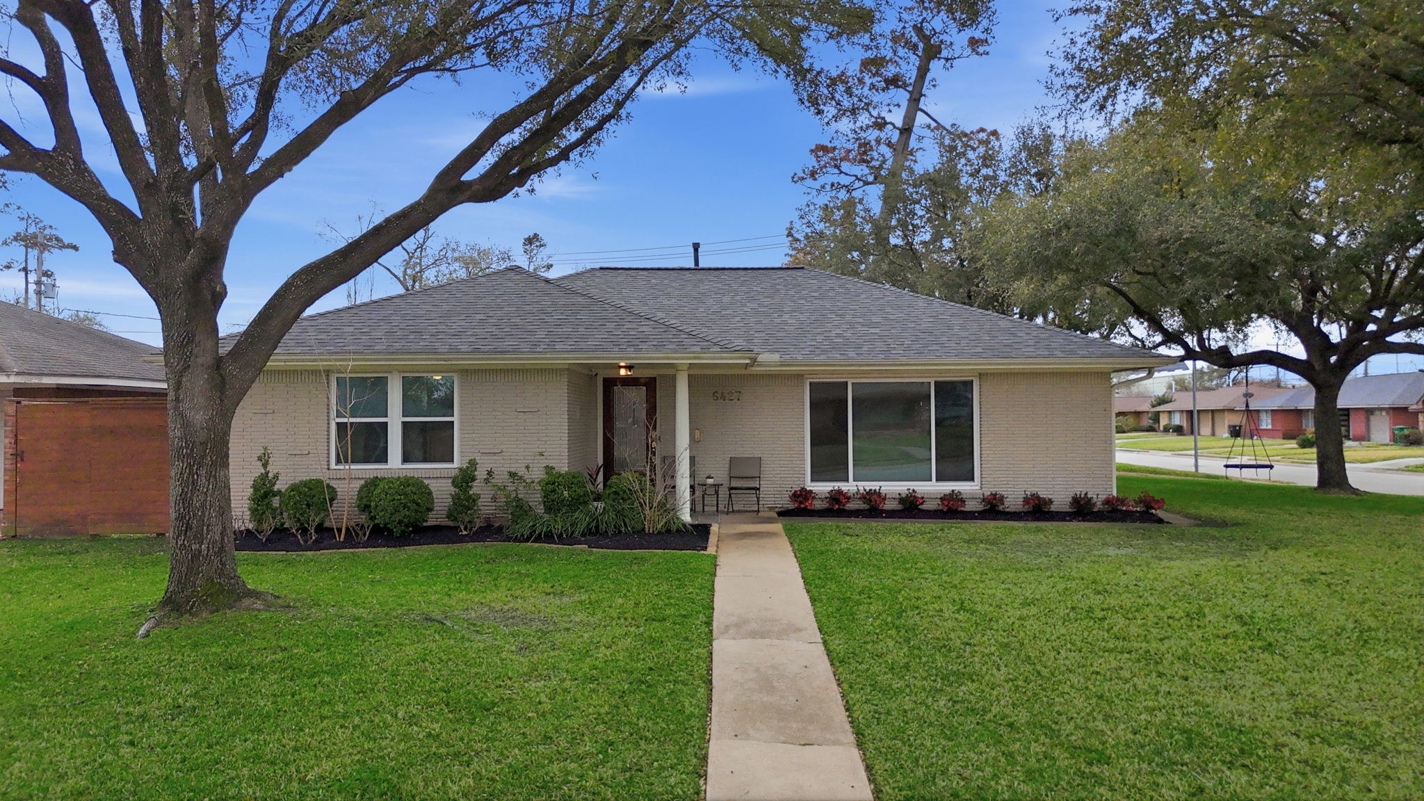 Charming single-story home with a well-maintained lawn and mature trees. Features a welcoming curb appeal with a paved walkway leading to the entrance.