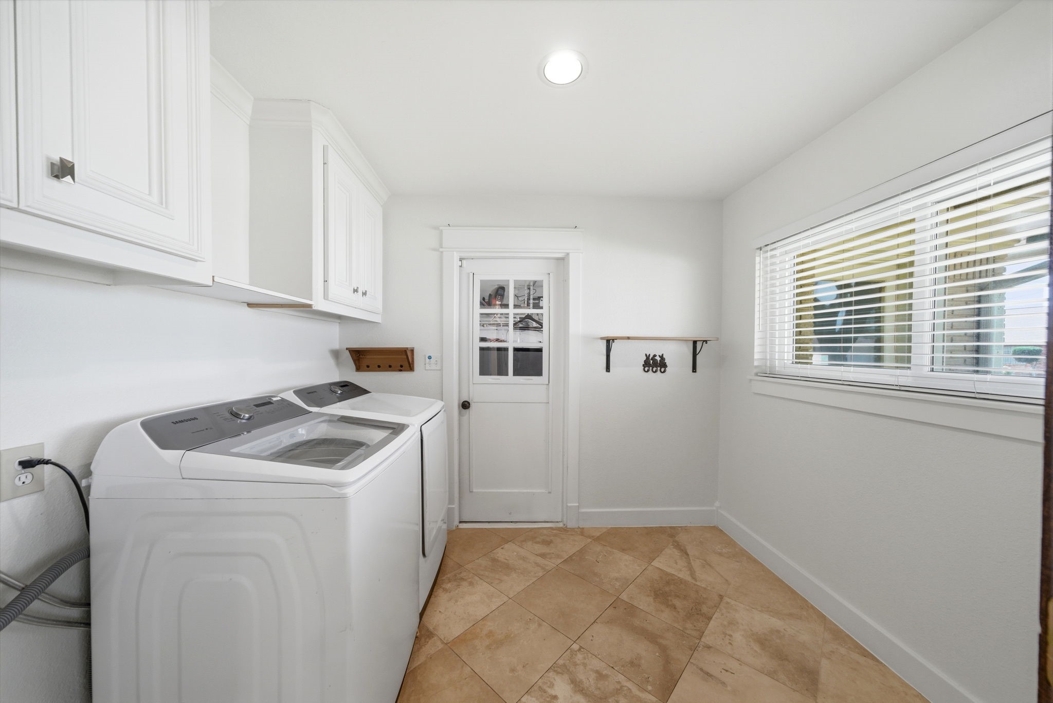 6427 Waltway Drive Houston, TX 77008 - Photo 12 of 37 This photo showcases a bright and spacious laundry room/mud room with modern appliances, white cabinetry, and travertine flooring. A large window provides ample natural light and the door leads to the garage.