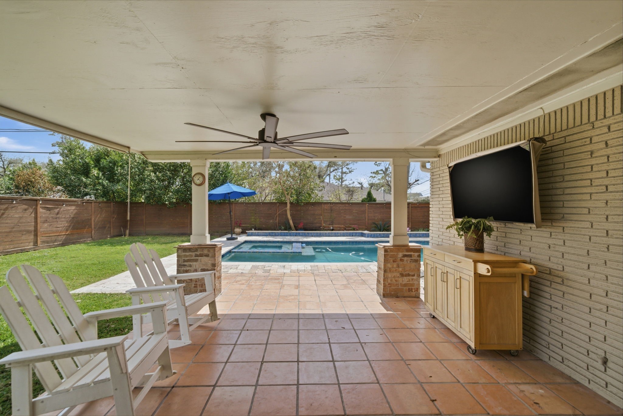 6427 Waltway Drive Houston, TX 77008 - Photo 15 of 37 Step outside to a covered outdoor patio with a ceiling fan, featuring a tiled floor and a wall-mounted TV. The space overlooks a well-maintained backyard with a swimming pool and privacy fence, perfect for relaxation and entertainment.