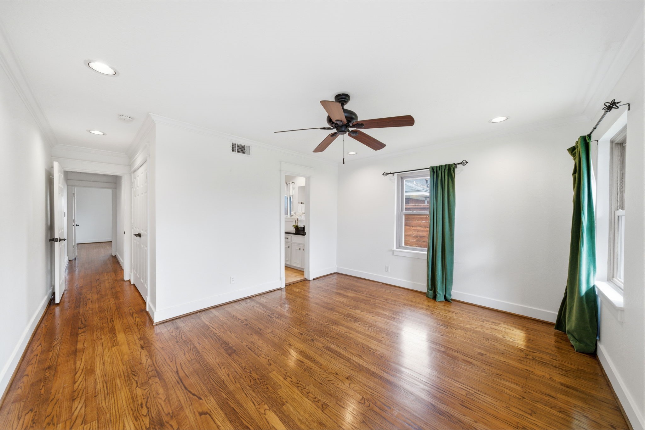 6427 Waltway Drive Houston, TX 77008 - Photo 22 of 37 Bright, airy room with polished hardwood floors and white walls. Features a ceiling fan, recessed lighting, and large windows, offering a cozy, inviting bedroom.
