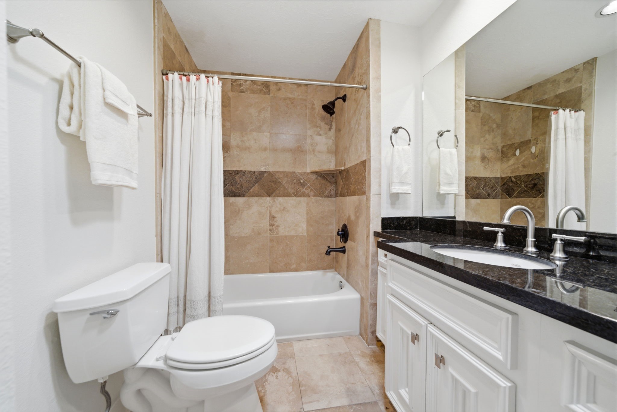 6427 Waltway Drive Houston, TX 77008 - Photo 29 of 37 This hall bathroom featuring a white vanity with black granite countertop, under mount sink, and elegant faucets. It includes a bathtub with a tiled tub/shower. The neutral tones create a clean and inviting atmosphere.