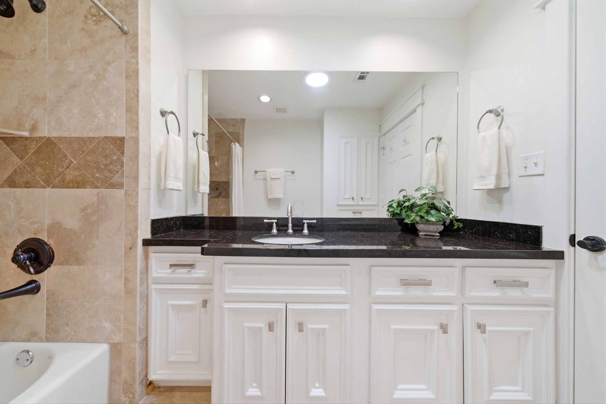6427 Waltway Drive Houston, TX 77008 - Photo 30 of 37 This bathroom features elegant beige tiles, a sleek black countertop, and white cabinetry. A large mirror adds depth, and the room is well-lit with recessed lighting and tube light that brings in natural light.