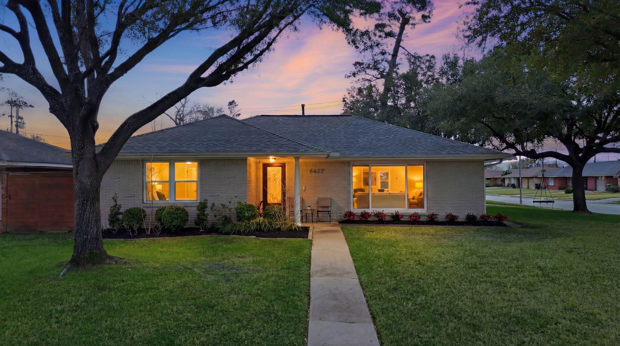 6427 Waltway Drive Houston, TX 77008 - Photo 36 of 37 Charming single-story home with a welcoming pathway, nestled on a corner lot. It features a well-maintained lawn and mature trees, highlighted by warm, inviting interior lights.