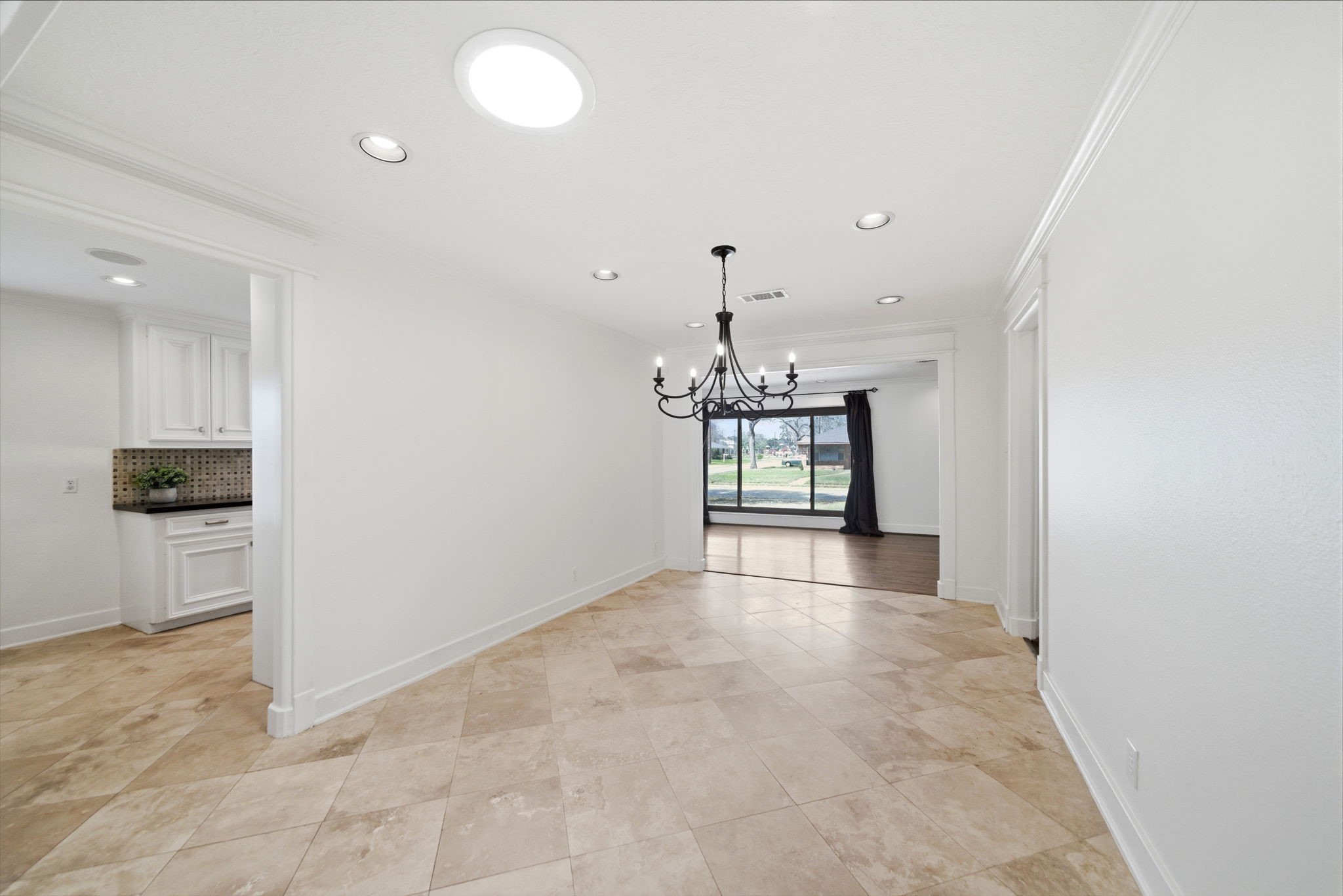 6427 Waltway Drive Houston, TX 77008 - Photo 7 of 37 Bright and spacious dining area with travertine flooring, recessed lighting, and a classic chandelier. It connects to a kitchen with white cabinetry and features a large window offering a view of the outdoors.
